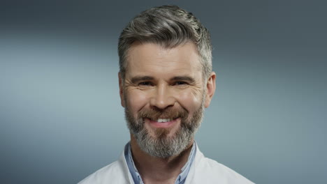 Portrait-shot-of-the-Caucasian-good-looking-grey-haired-man-doctor-with-a-beard-smiling-cheerfully-to-the-camera.-Close-up.